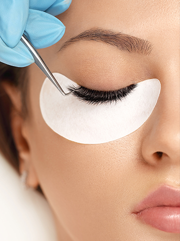 An extension being placed with tweezers, under-eye pad in position